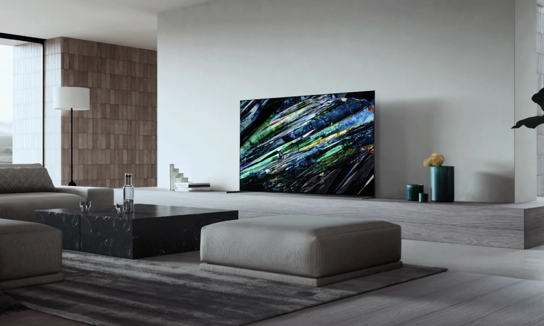 Marketingfoto des Sony A95L-Fernsehers in einem vornehmen Wohnzimmer.  Moderne graue Ästhetik mit eleganten Möbeln und raumhohen Fenstern auf der linken Seite.