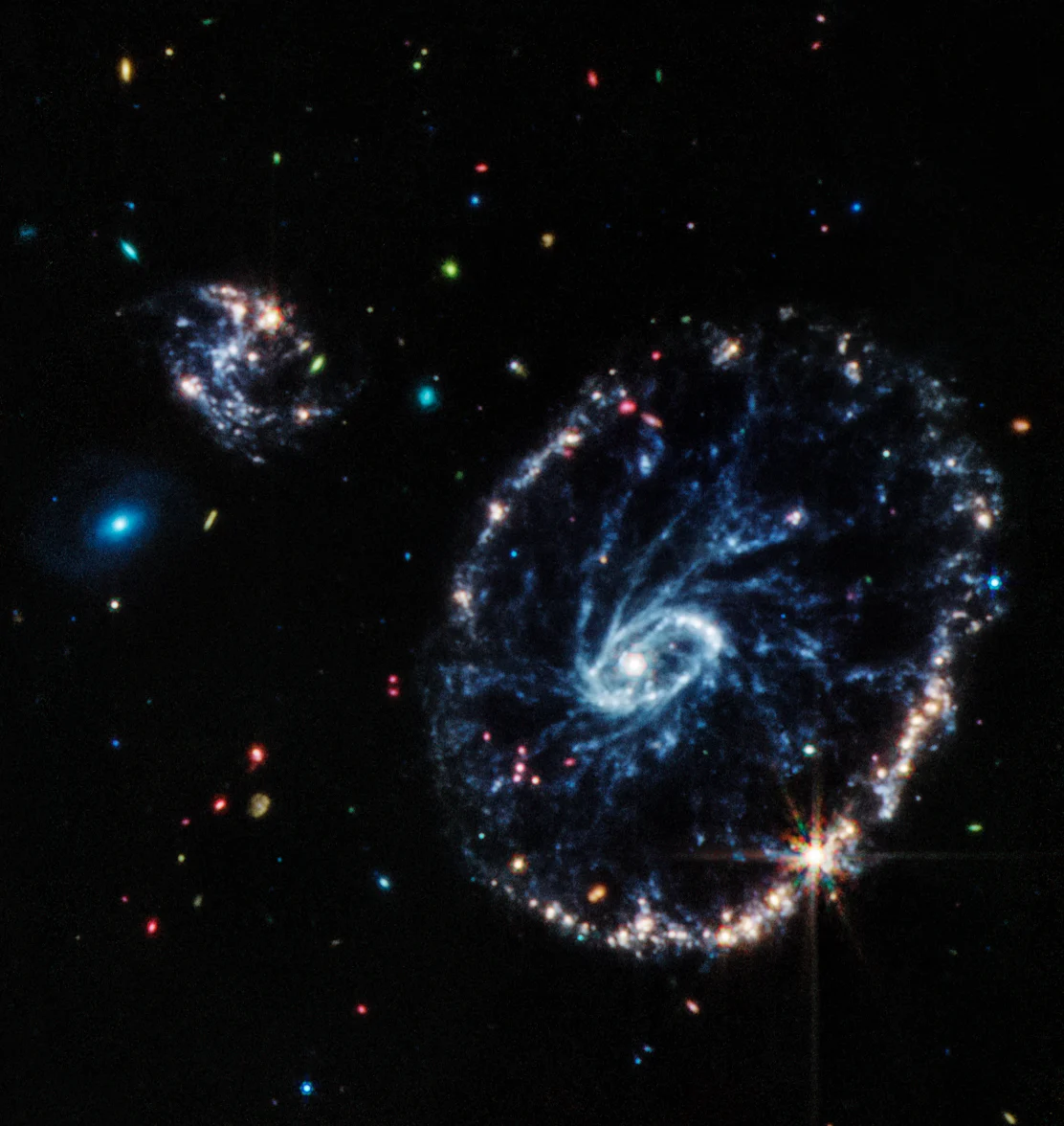 This image from Webb’s Mid-Infrared Instrument (MIRI) shows a group of galaxies, including a large distorted ring-shaped galaxy known as the Cartwheel. The Cartwheel Galaxy, located 500 million light-years away in the Sculptor constellation, is composed of a bright inner ring and an active outer ring. While this outer ring has a lot of star formation, the dusty area in between reveals many stars and star clusters.