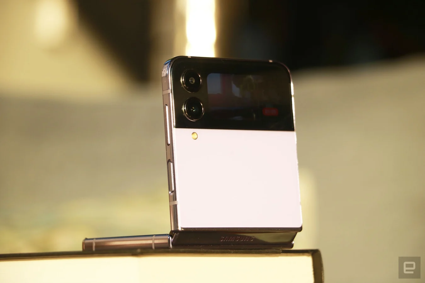 Das Galaxy Z Flip 4 halb zusammengeklappt und auf einem Buch gestützt, wobei das Cover-Display nach außen zeigt und das Bild von etwas zeigt, das aufgezeichnet wird.