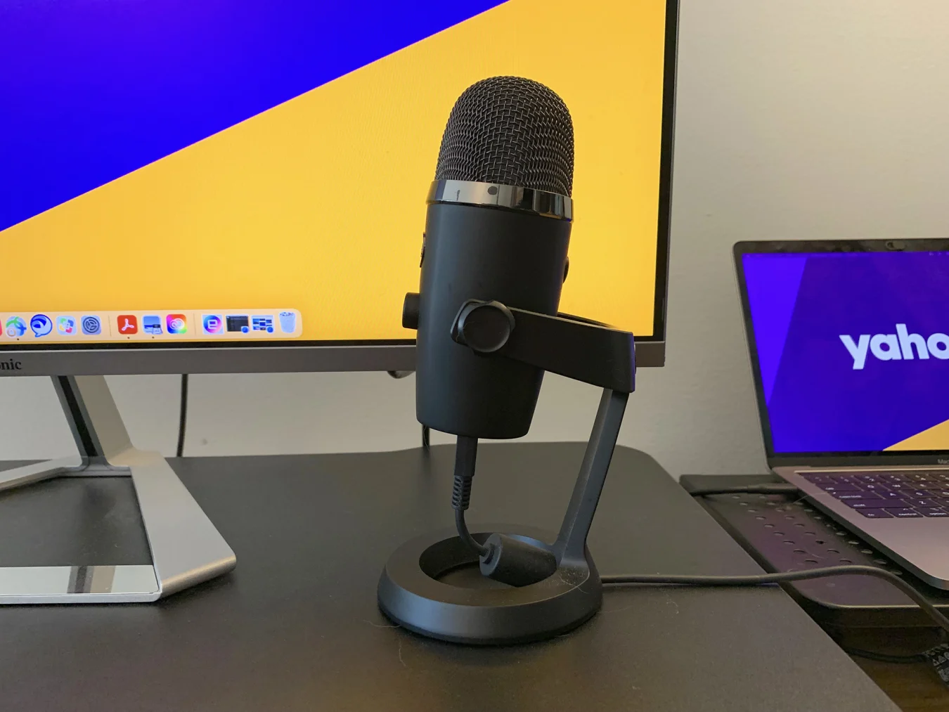 The Blue Yeti Nano Microphone on a black tabletop in front of a laptop and computer monitor.