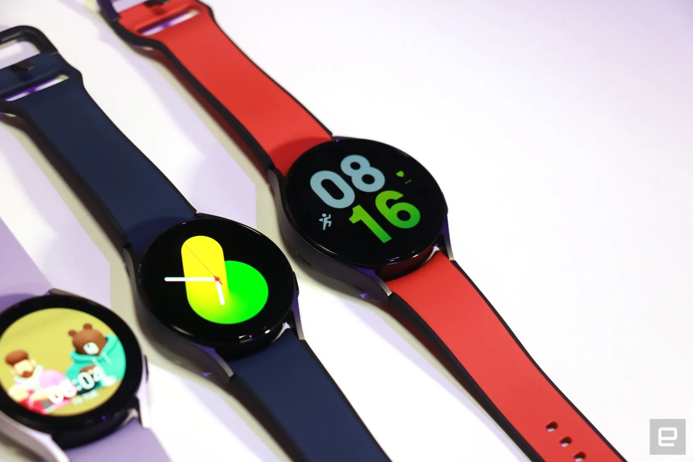 A trio of Galaxy Watch 5 units on a table, with purple, blue and red straps from left to right.