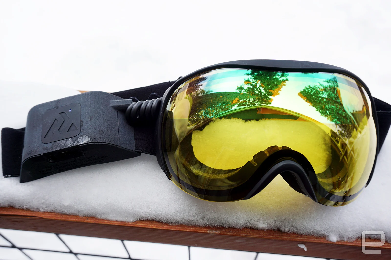 Ski goggles with yellow lenses and a battery pack on the side of the strap.                               