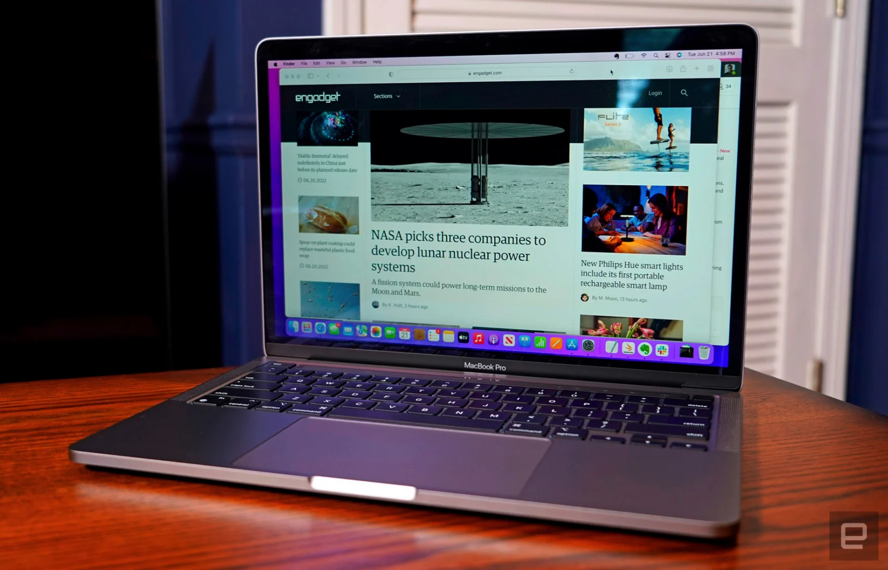 The MacBook Pro 13-inch M2 (2022) sits open on a wooden dining room tabletop in a room with blue walls and white doors.
