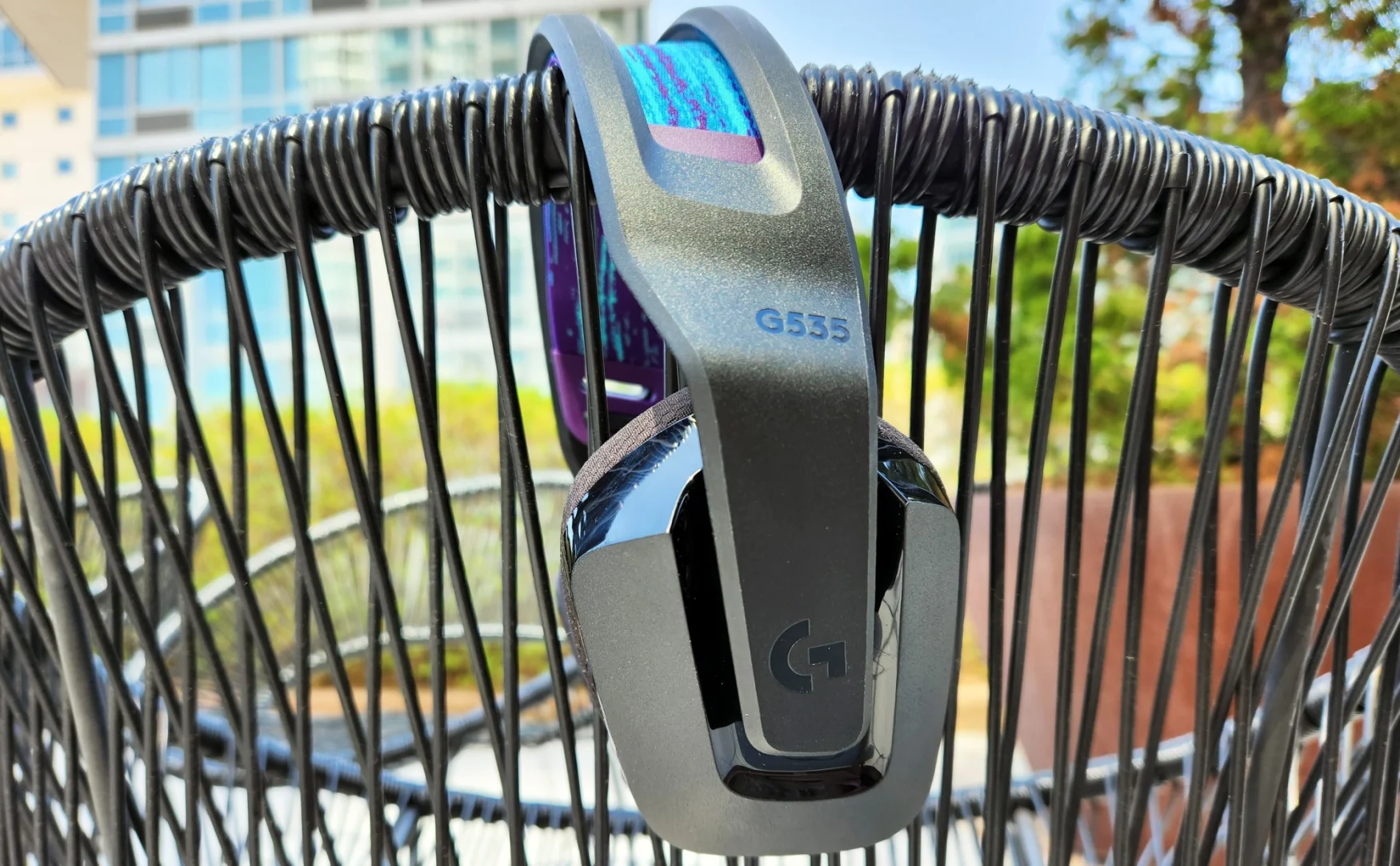 Logitech's G535 wireless gaming headset rests on top of a wicker chair on a patio outdoors.