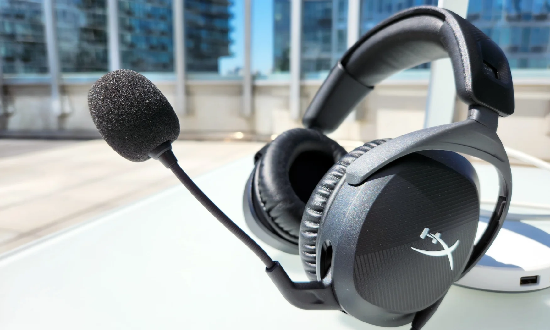 A black gaming headset with a built-in boom microphone, the HyperX Cloud Stinger 2, rests on a white table in an outdoors setting.