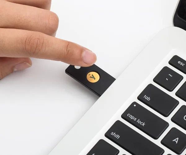 Yubico YubiKey NFC 5 security key in a laptop port with a human finger reaching to touch it.