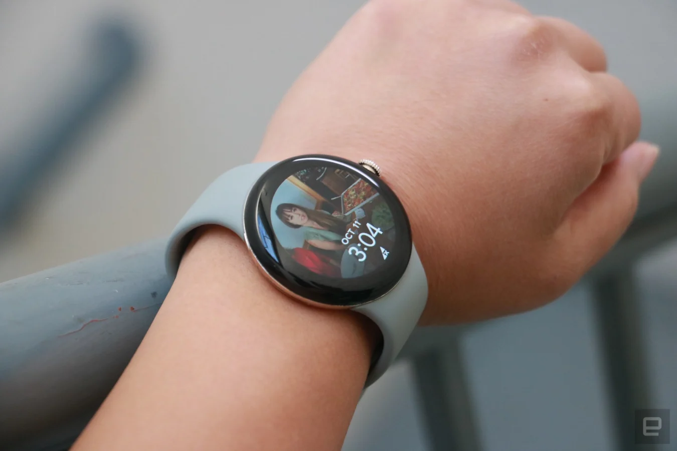 Die Pixel Watch am Handgelenk einer Person mit einem Foto als Hintergrund.