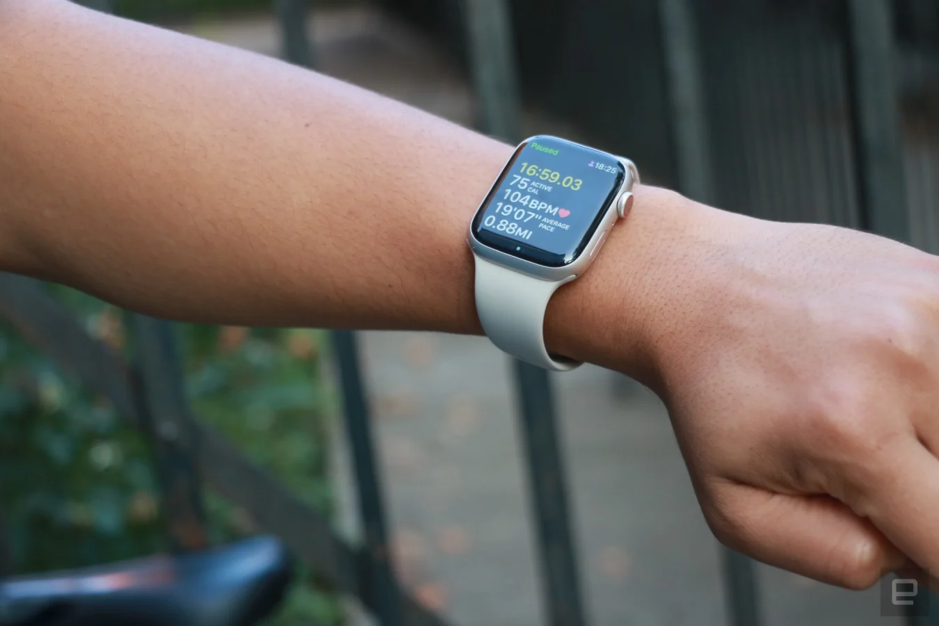 The Apple Watch Series 8 on the wrist of an arm held in the air with a bicycle seat in the background.