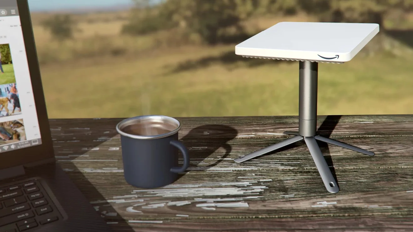 An Amazon Project Kuiper satellite internet kiosk sits on a table outside, alongside a cup and laptop.