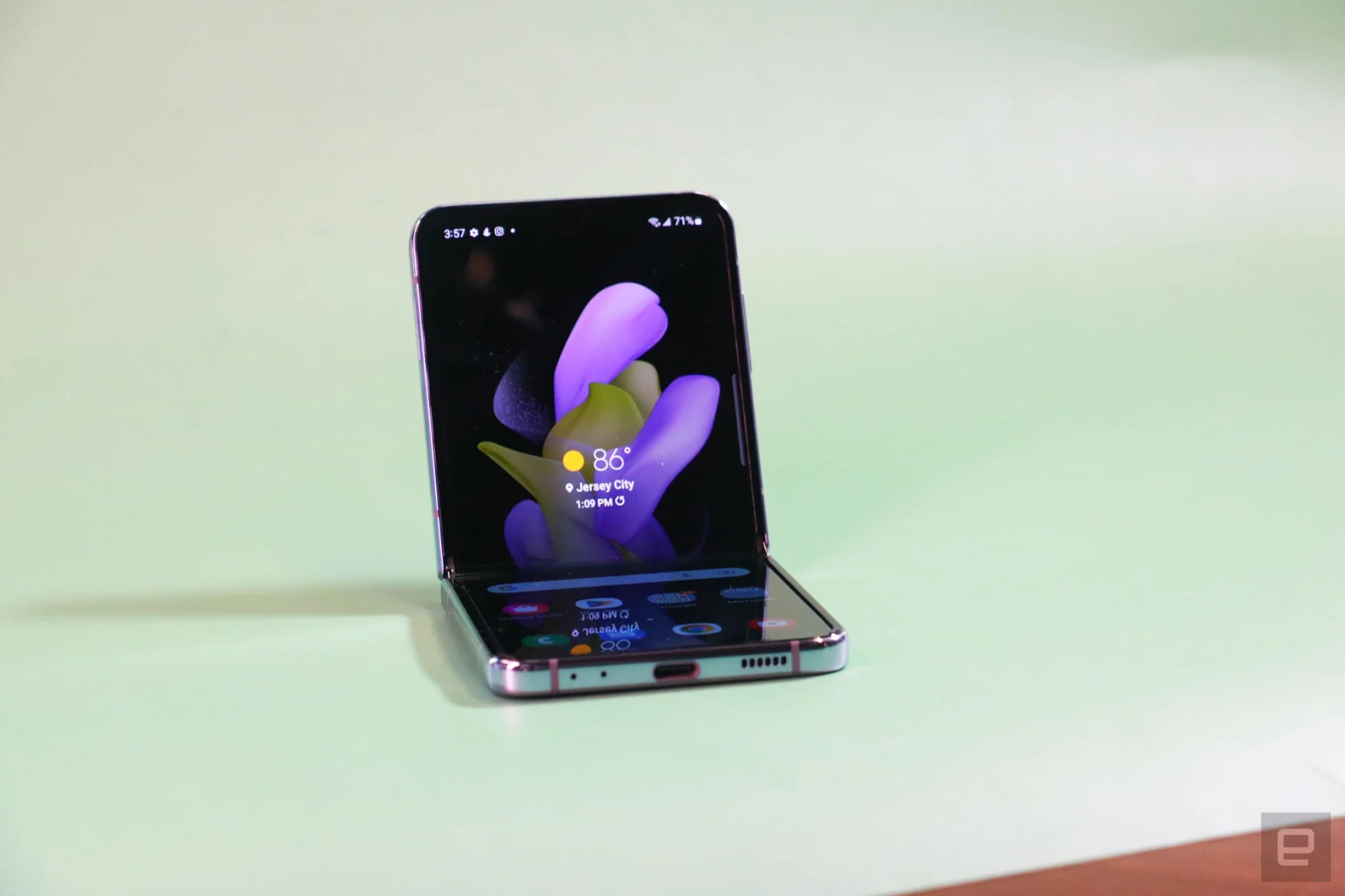 The Galaxy Z Flip 4 half folded and sitting up on a green surface with its screen facing out.
