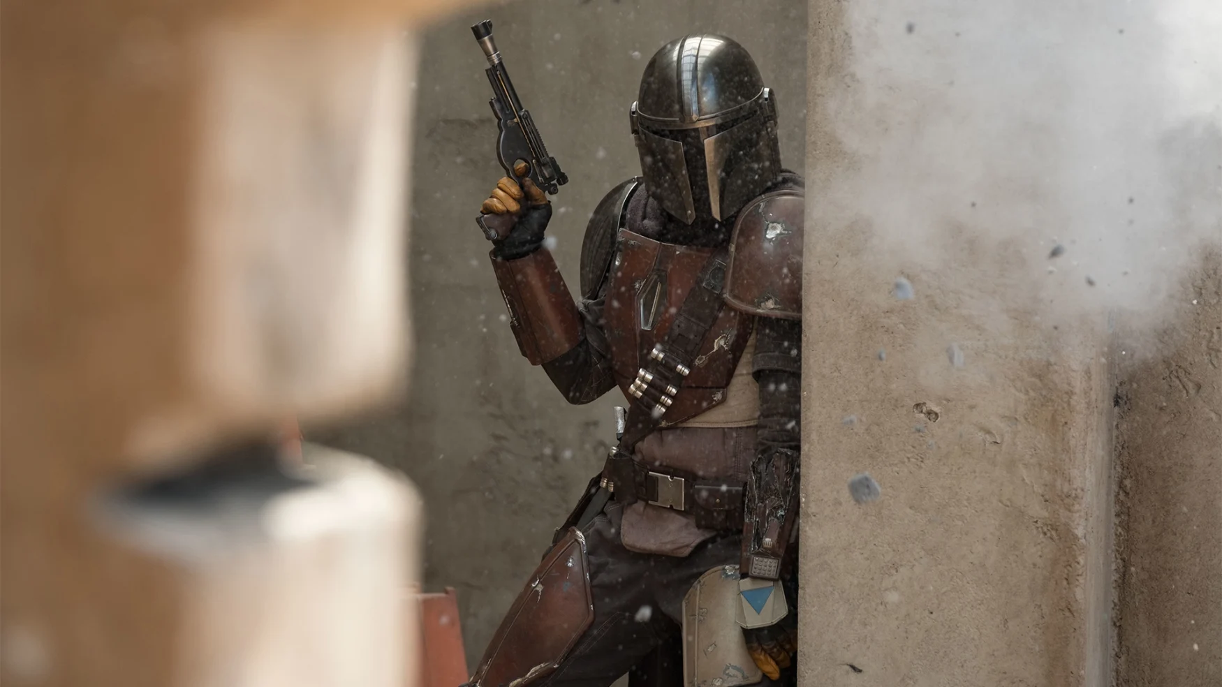 Media image from “The Mandalorian,” featuring the title character holding a blaster while taking cover behind a corner.