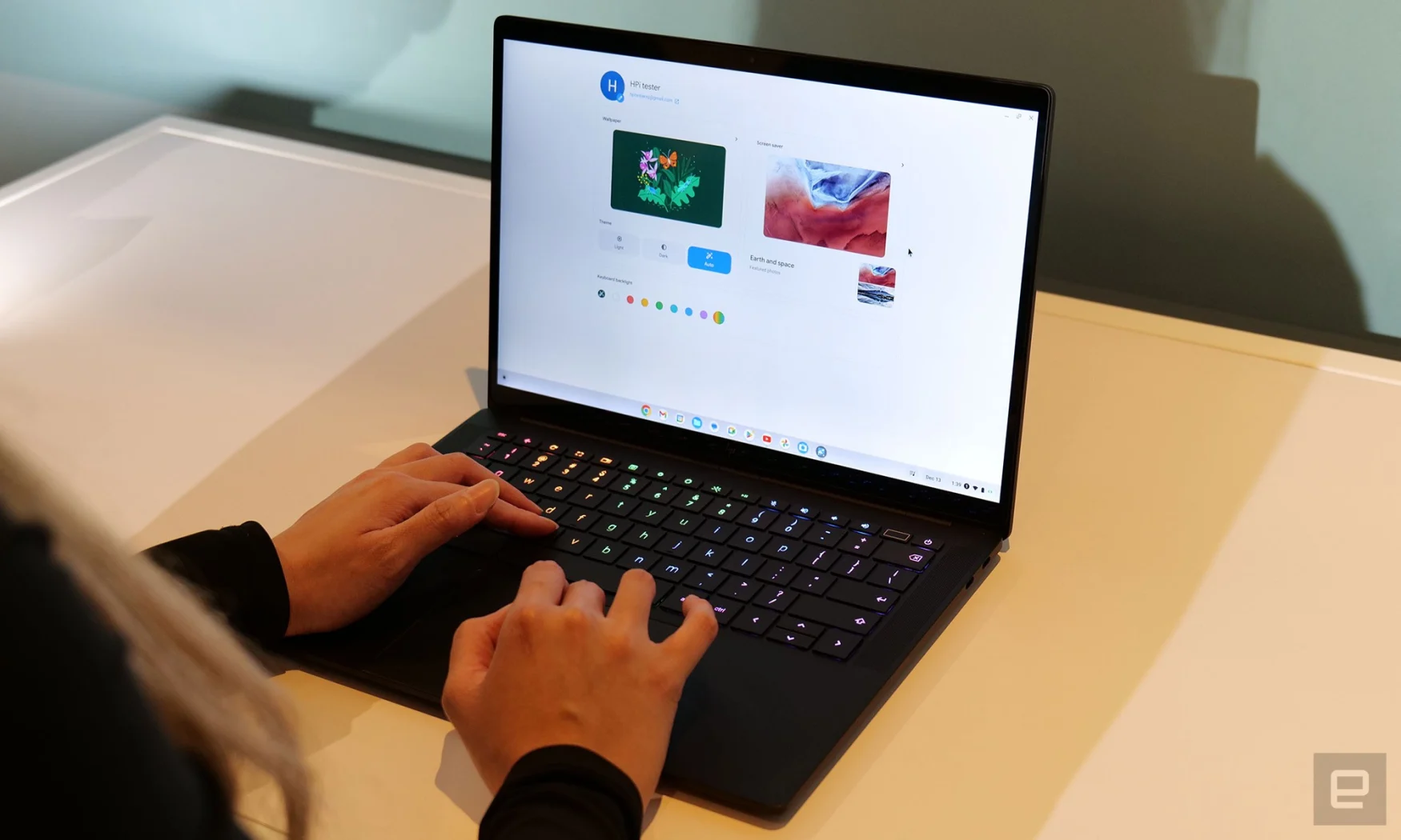 Eine Person, die auf einem schwarzen HP Dragonfly Pro Chromebook tippt.  Die Tasten sind in Regenbogenfarben hintergrundbeleuchtet, und der Bildschirm zeigt die Seite zur Auswahl der Hintergrundbilder.