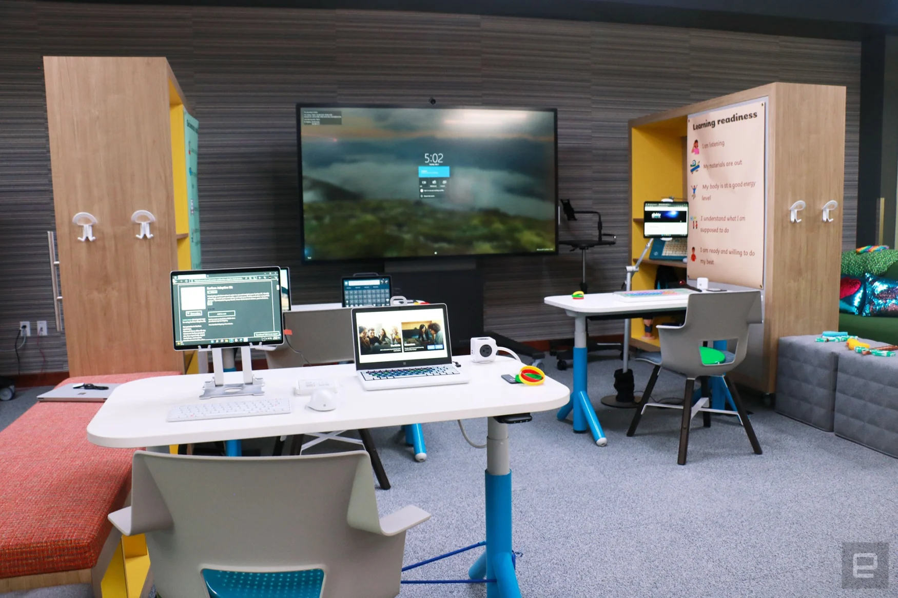 The faux classroom inside Microsoft's new Inclusive Tech Lab. Three tables are set up facing a Surface Hub and each table has assistive devices on it.