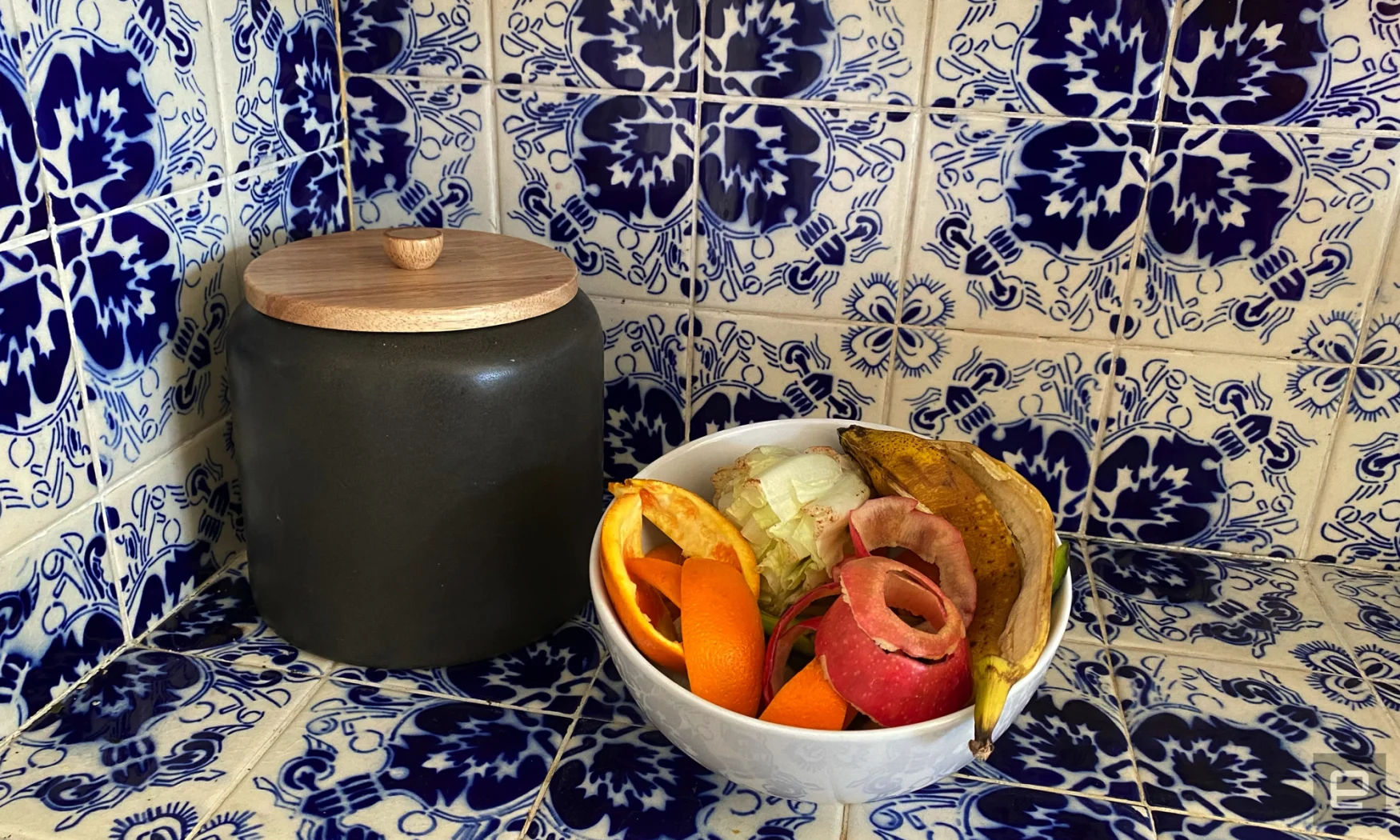 A bowl of food scraps sits on a blue and white countertop next to a ceramic canister. 