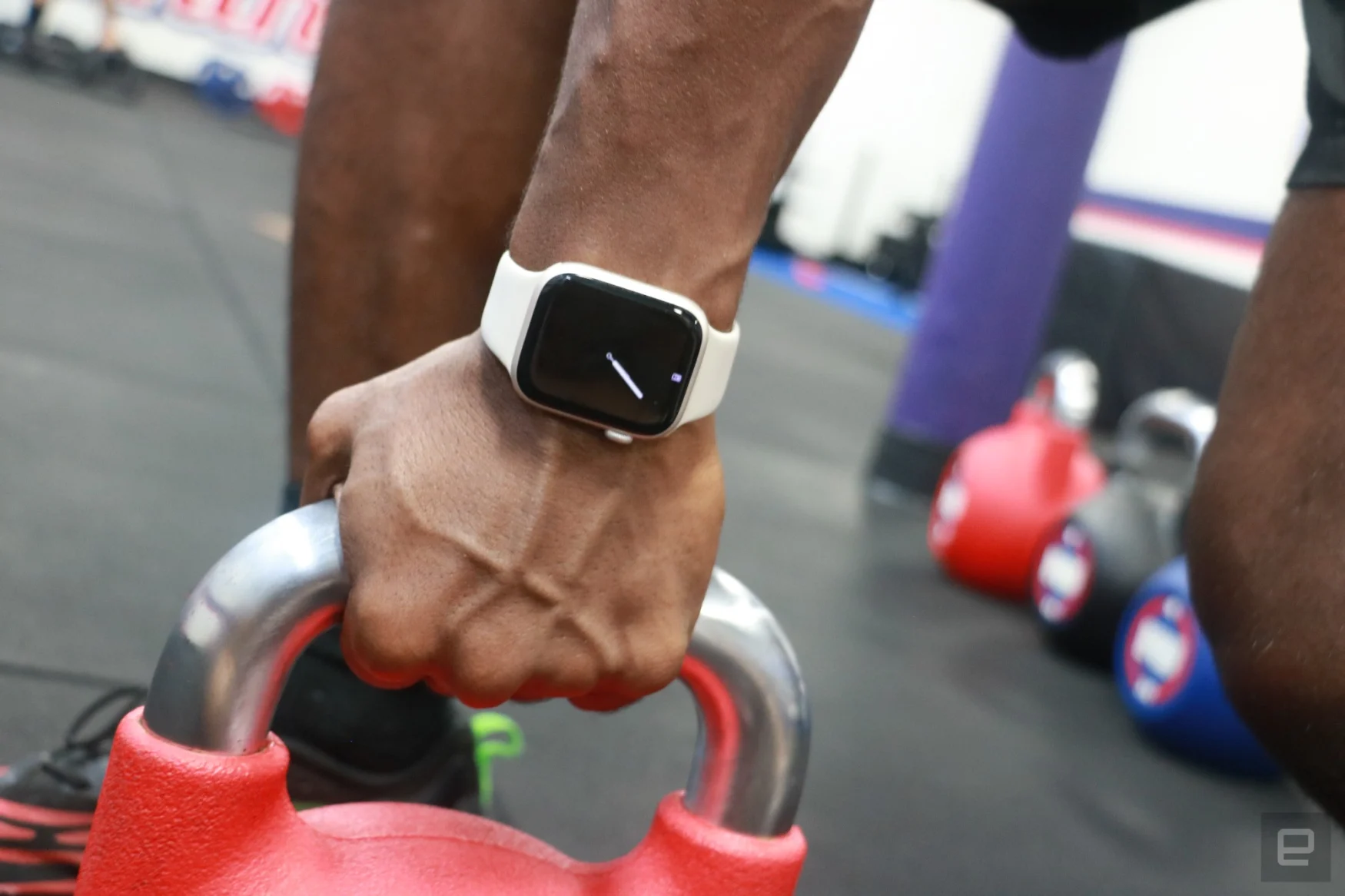 An Apple Watch Series 8 on the wrist of a person gripping a red kettlebell, showing its Always On Display.