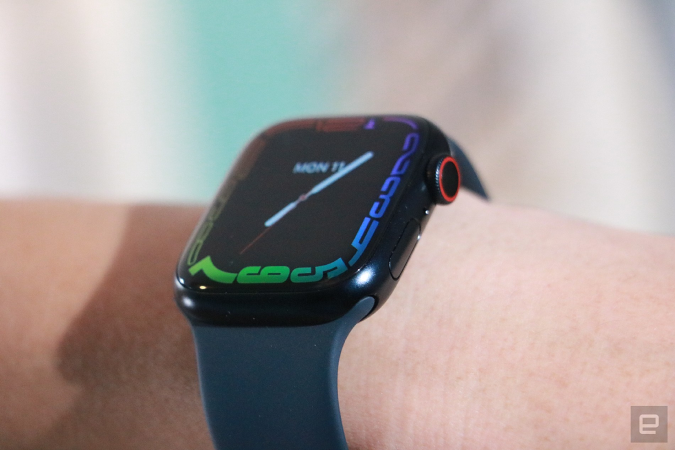 An off-angle view of the Apple Watch Series 7 on a person's wrist, showing the screen's refracted edge and the watch's dial and button.