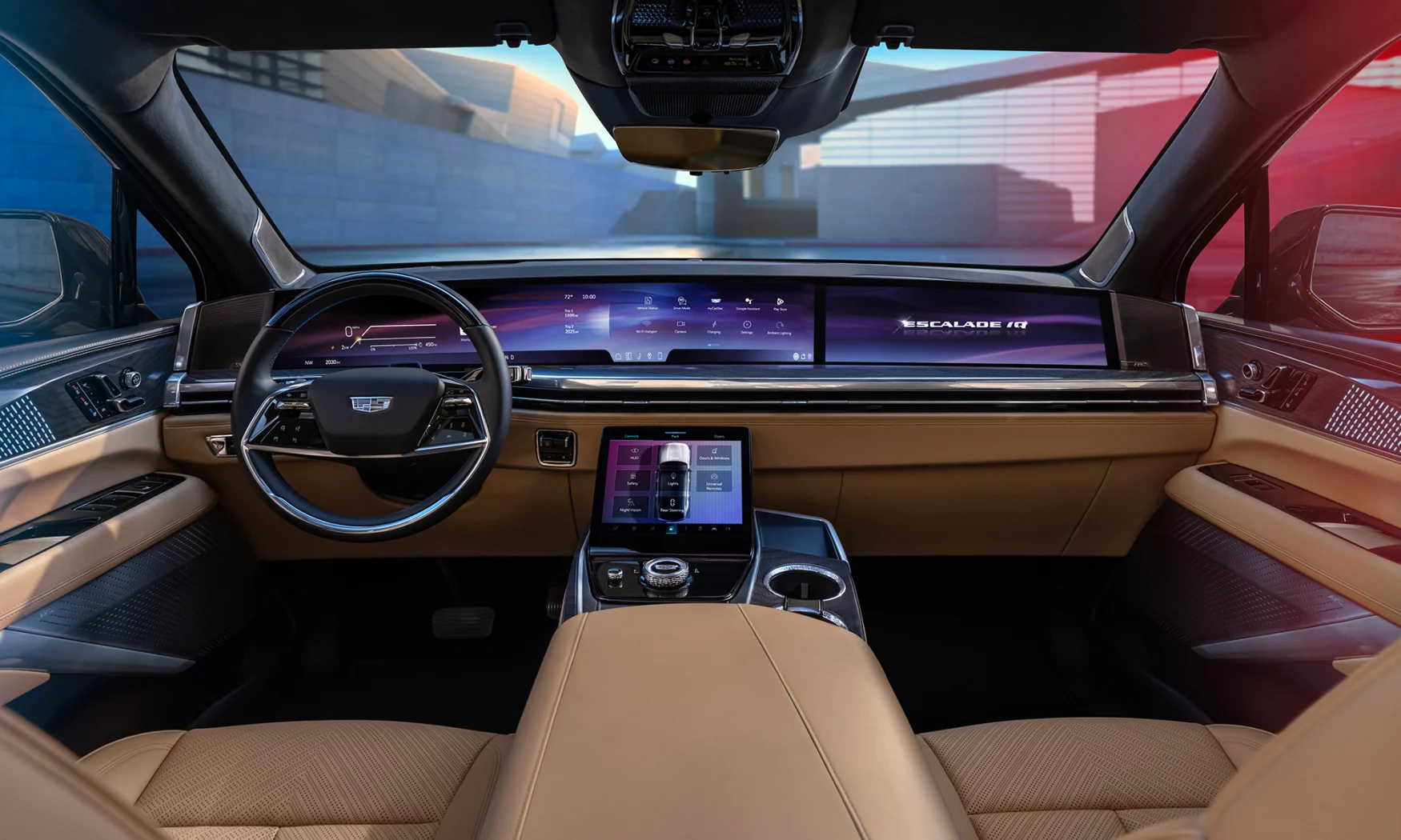 View from the center console of the 2025 Cadillac Escalade IQ. It has brown leather seats and a 55-inch dual-screen LED display on the dash. Daylight with city buildings visible through the winshield.