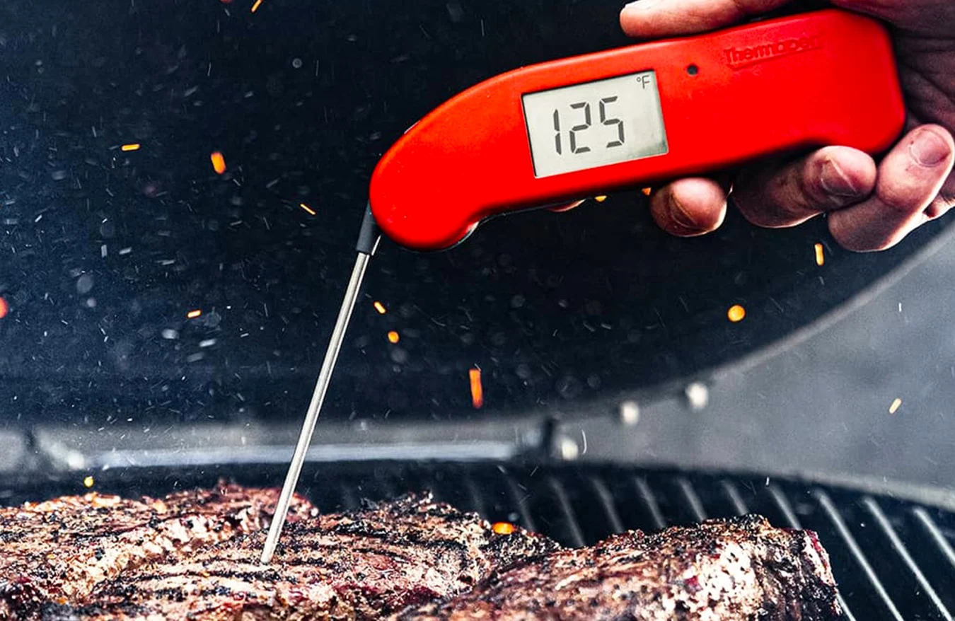 The ThermoWorks Thermapen One thermometer checking the temperature of a piece of meat cooking on a grill.