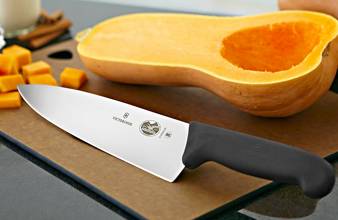 A Victorinox Chef Knife on a cutting board next to a sliced squash.