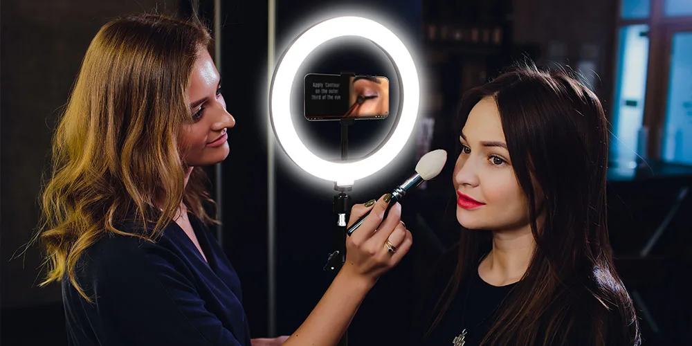 Press image of the U-STREAM Home Streaming Studio and 10-inch Ring Light & Tripod, being used by a makeup artist on a female client.
