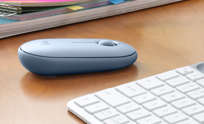 The Logitech Pebble mouse in light blue sitting on a desk next to a keyboard.