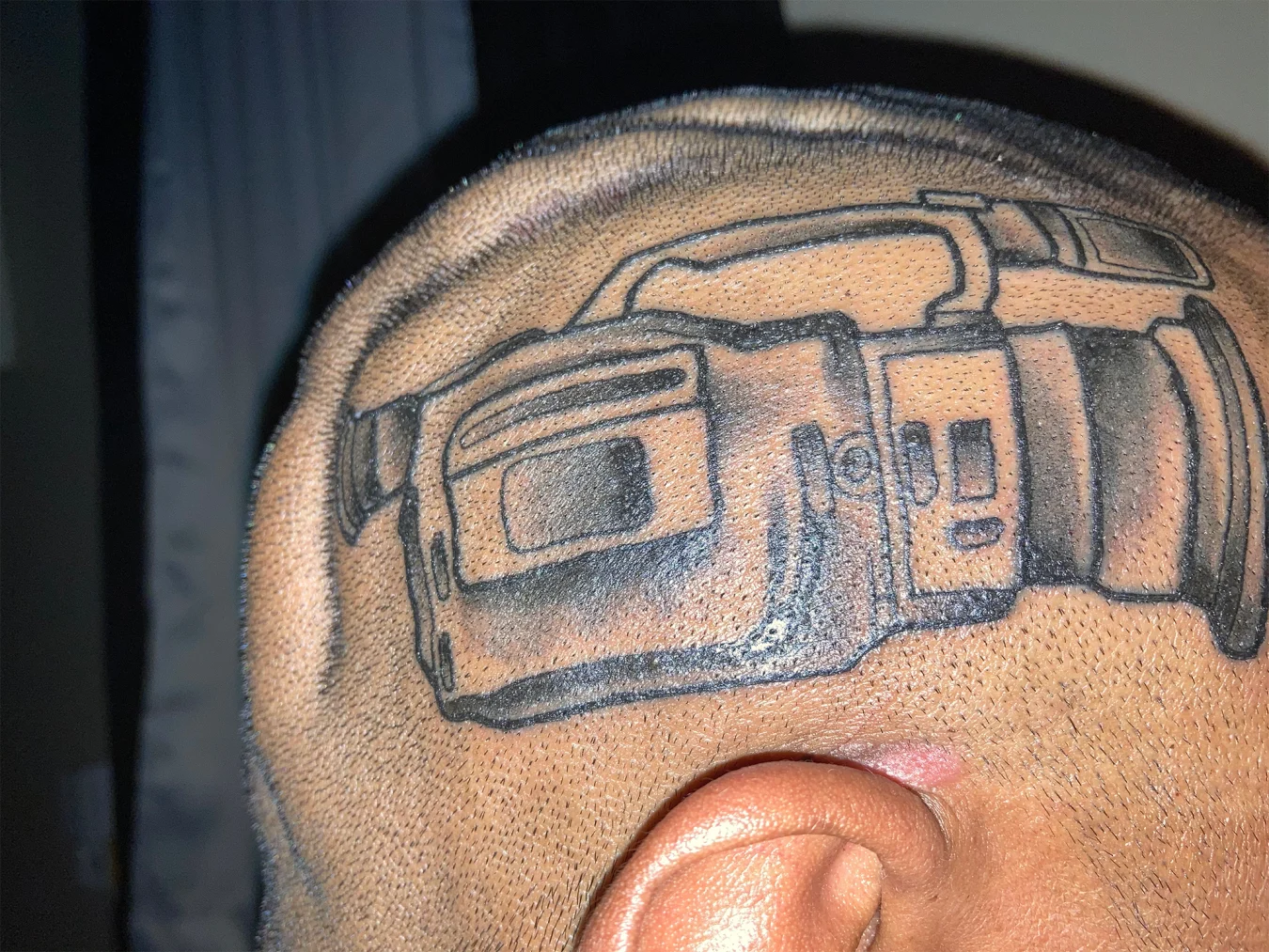 A man with a tattoo of a Sony VX1000 video camera on his head.