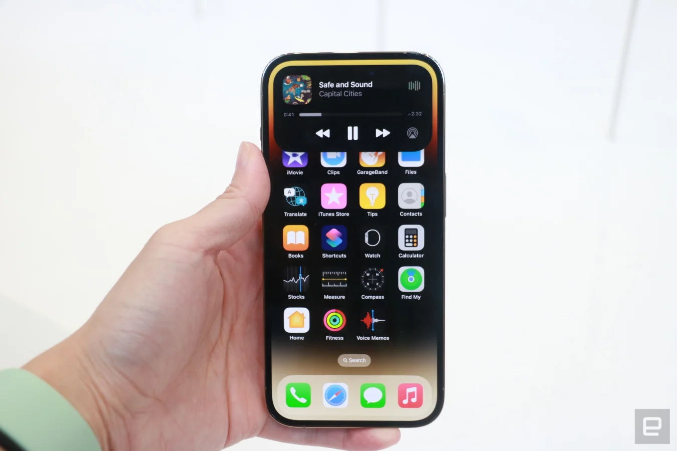 The iPhone 14 Pro held against a white background, with the new dynamic island cutout showing an Apple Music playback box.