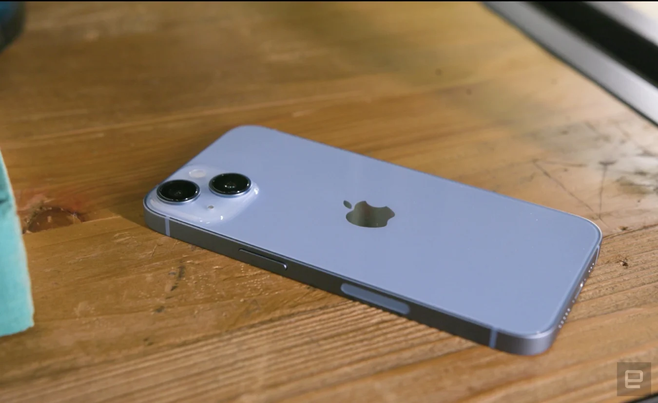 El iPhone 14 azul boca abajo sobre una superficie de madera, con el borde derecho hacia la cámara.