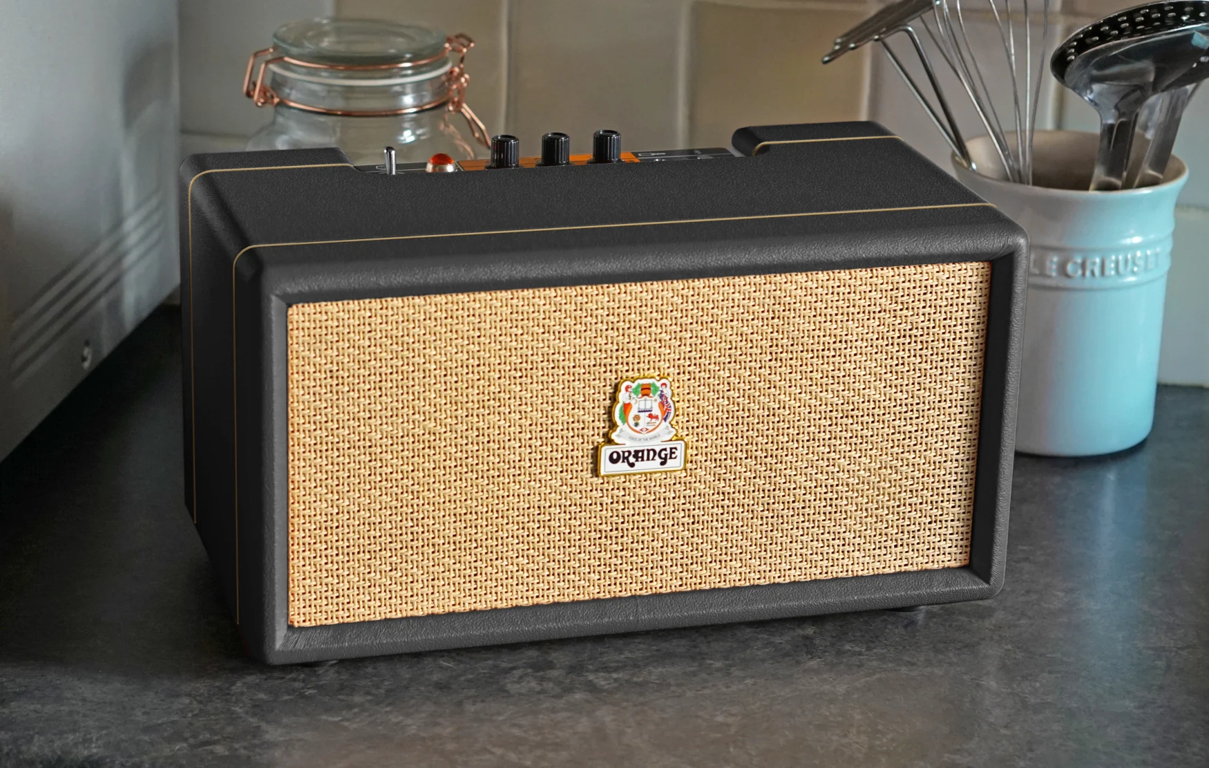 An Orange Amps Box-L wired Bluetooth talker  with a achromatic  exterior sits connected  a granite room  countertop.