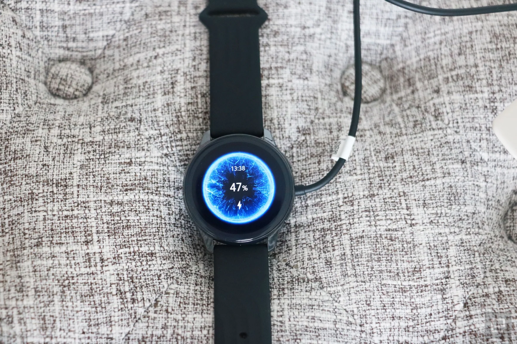 OnePlus Watch review photos. OnePlus Watch on a charger with display showing 47 percent battery and time at 1:38pm.