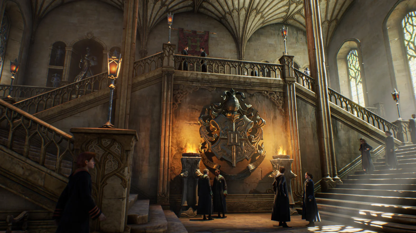 The main hall of Hogwarts fills the space, with students descending a double staircase, the top of which is large and lit by two bonfires on a pedestal.