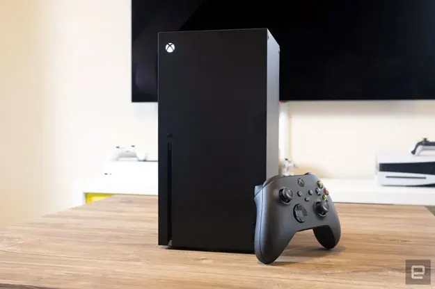 Image of the Xbox One Series X on a beechwood table in front of a big screen TV.