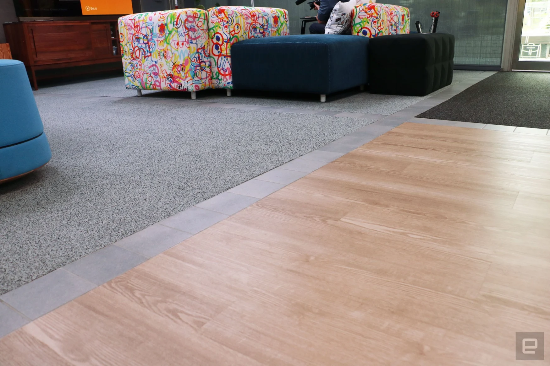 A shot of the floors at Microsoft's new Inclusive Tech Lab, with a light wood section, gray carpet section and dark carpet section in the frame. The areas are separated by a light gray stone tile.