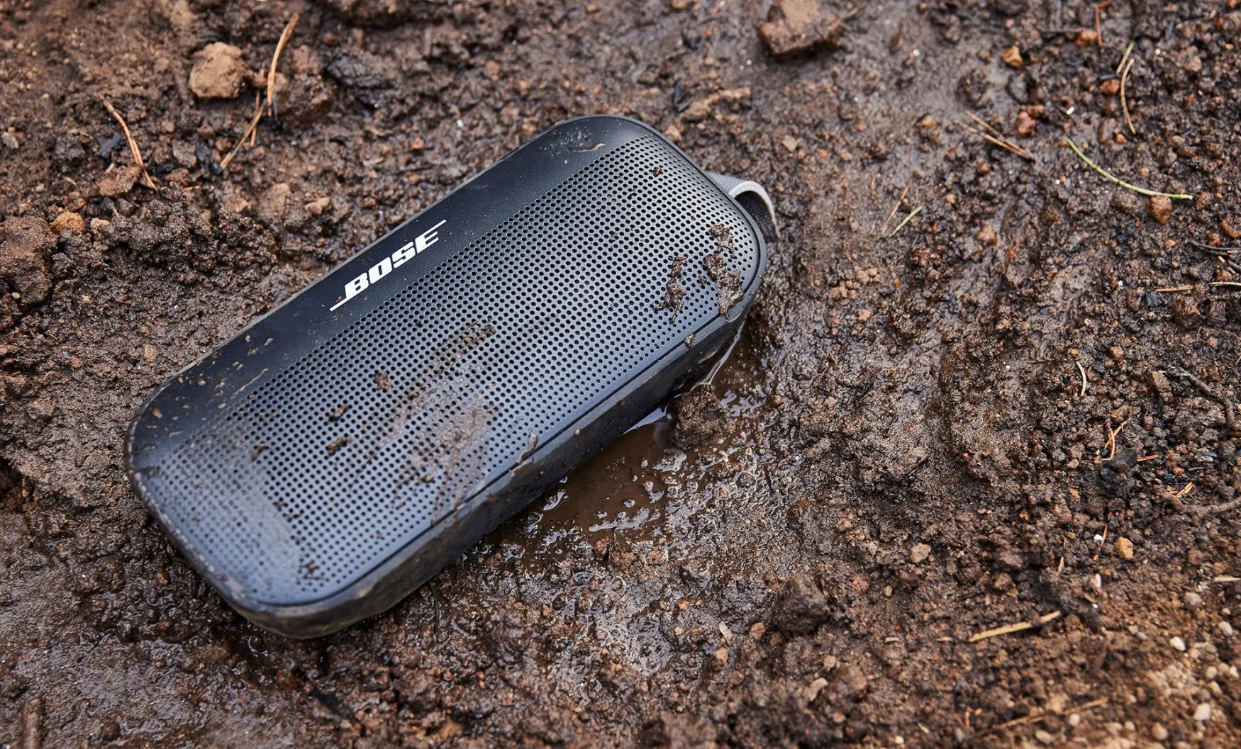 A Bose SoundLink Flex portable Bluetooth speaker in some mud.