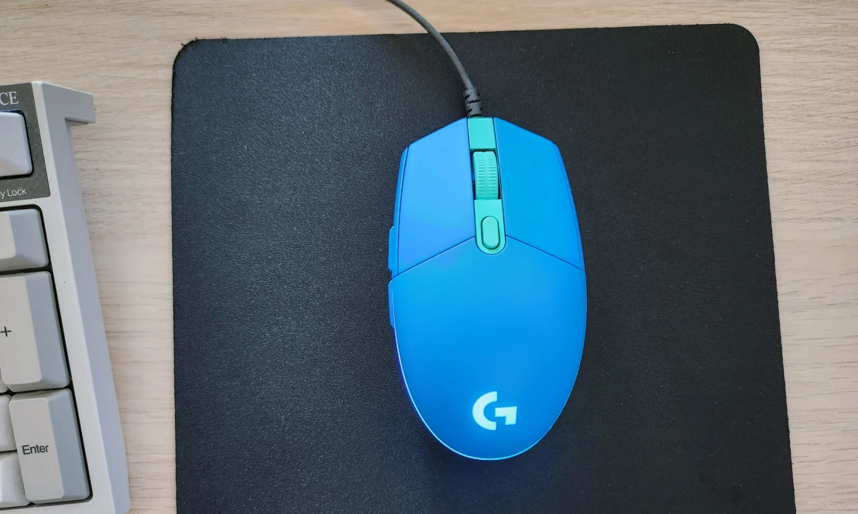 A blue Logitech G203 Lightsync gaming mouse rested on top of a black mouse pad on a desk.