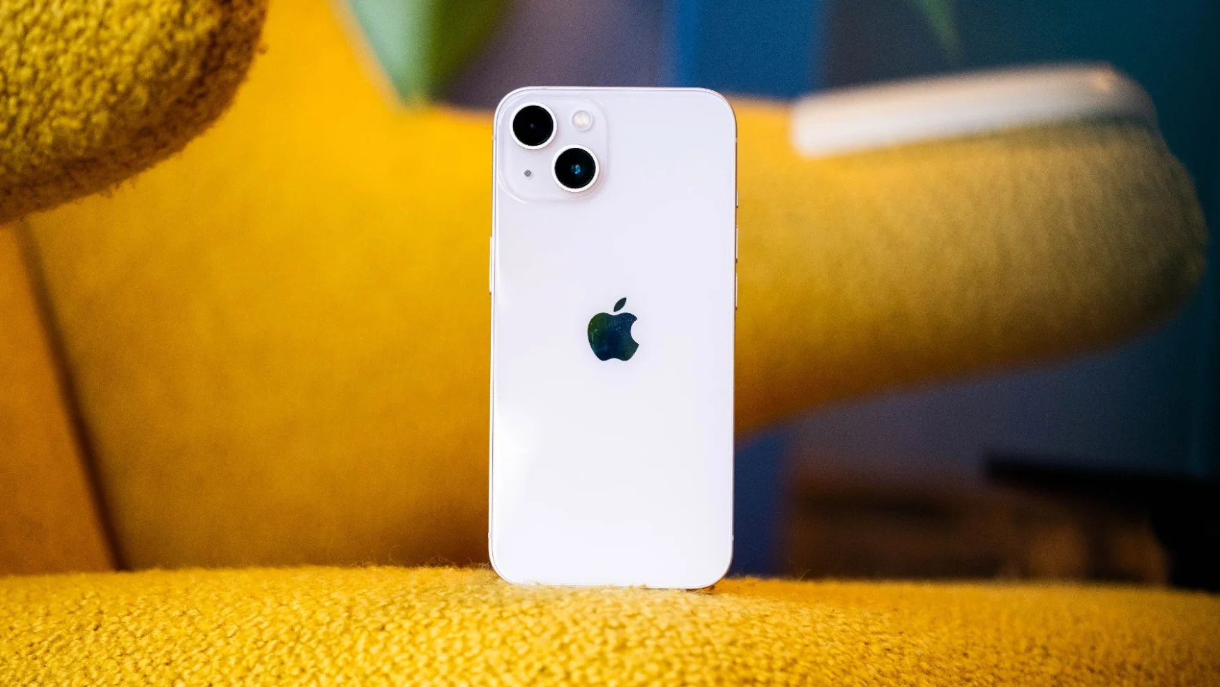 A pink iPhone 13 on a mustard-colored couch with its rear facing the camera.