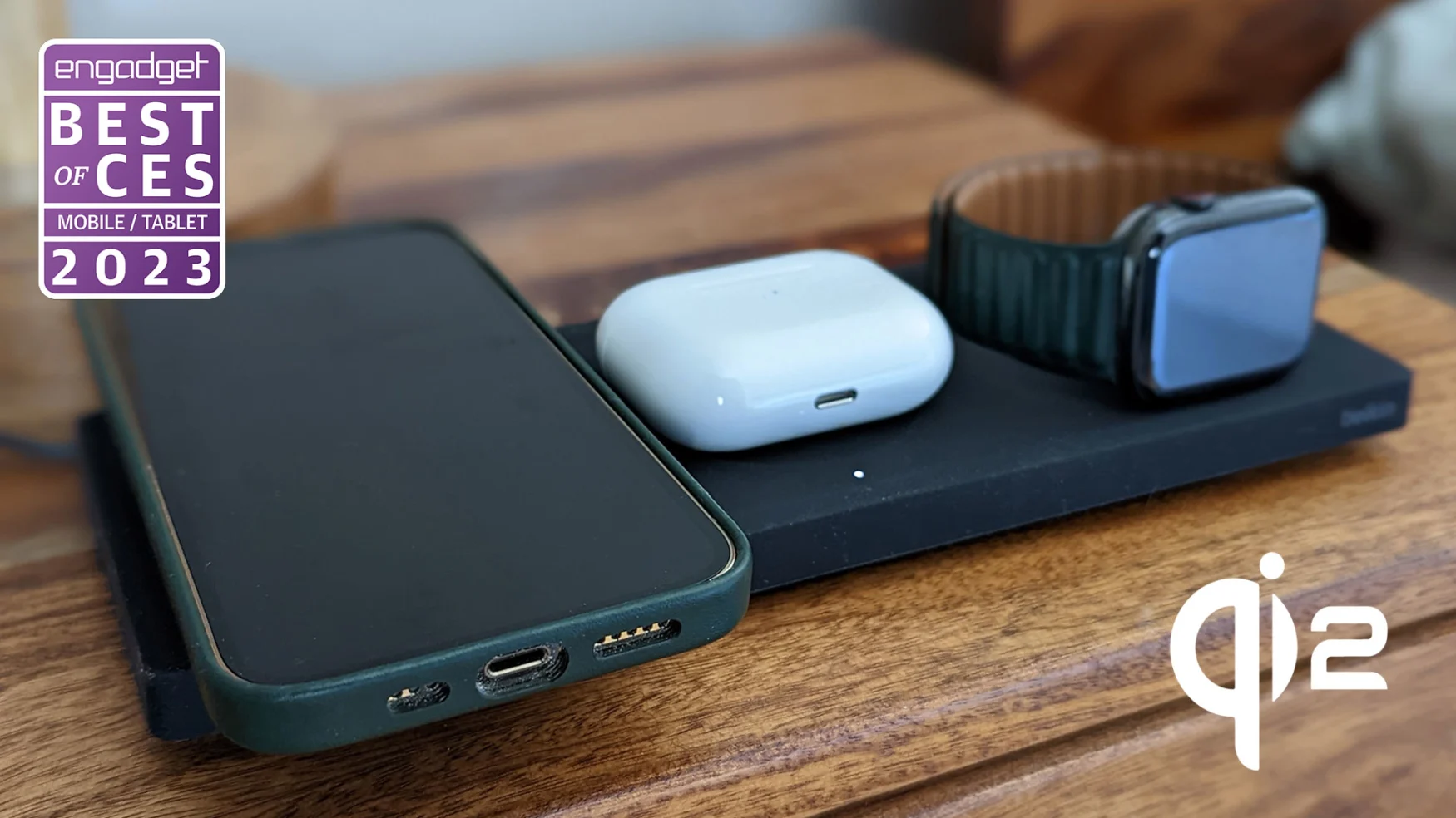 A Belkin wireless charger with a phone, AirPods case and Apple Watch charging on it sits on a wooden side table.