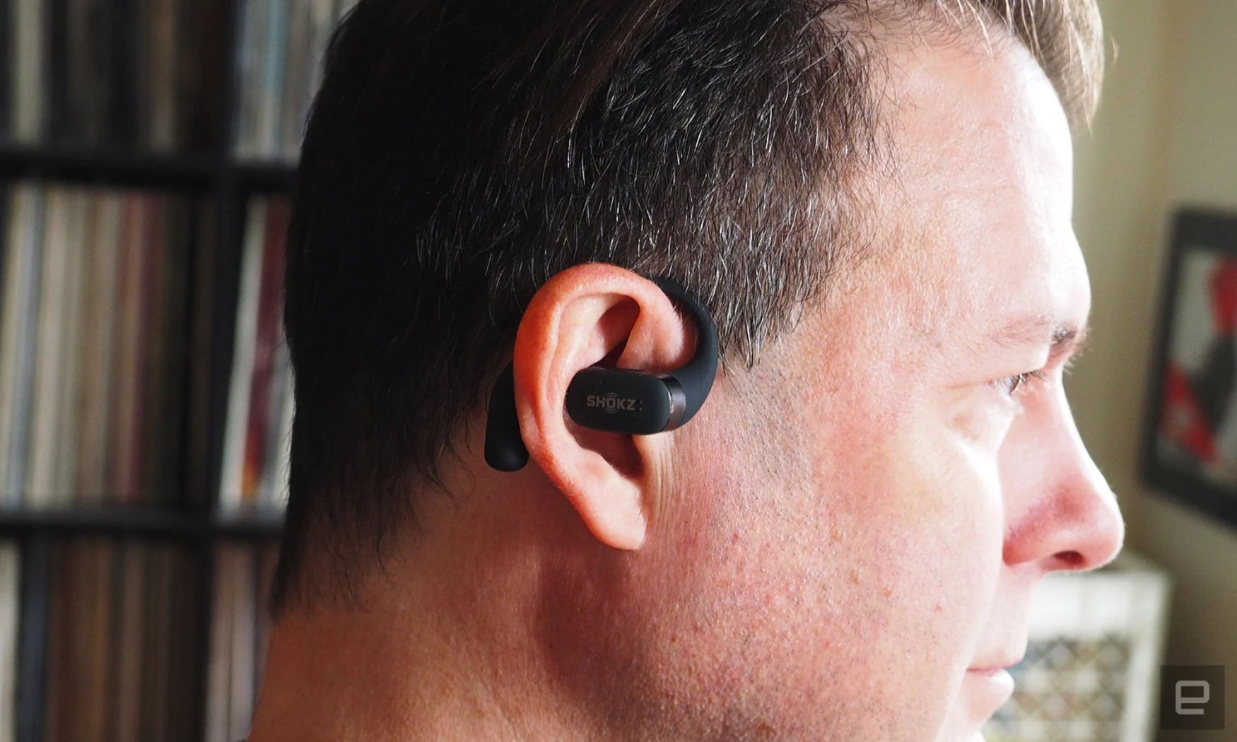Close-up images of the Shokz OpenFit open-ear buds in grey being worn by someone seen in profile.