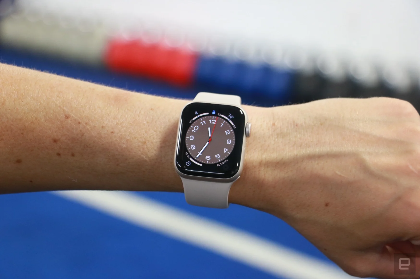 The Apple Watch SE (2022) on a person's wrist held up in front of a colorful row of kettlebells.