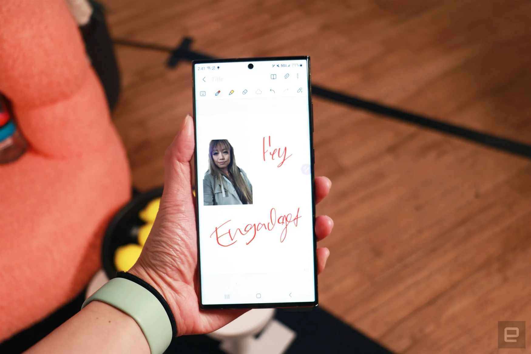 The Galaxy S23 Ultra held in a hand in mid-air showing the Samsung Notes app. On the canvas is a cutout of a woman on the top left and the handwritten words 