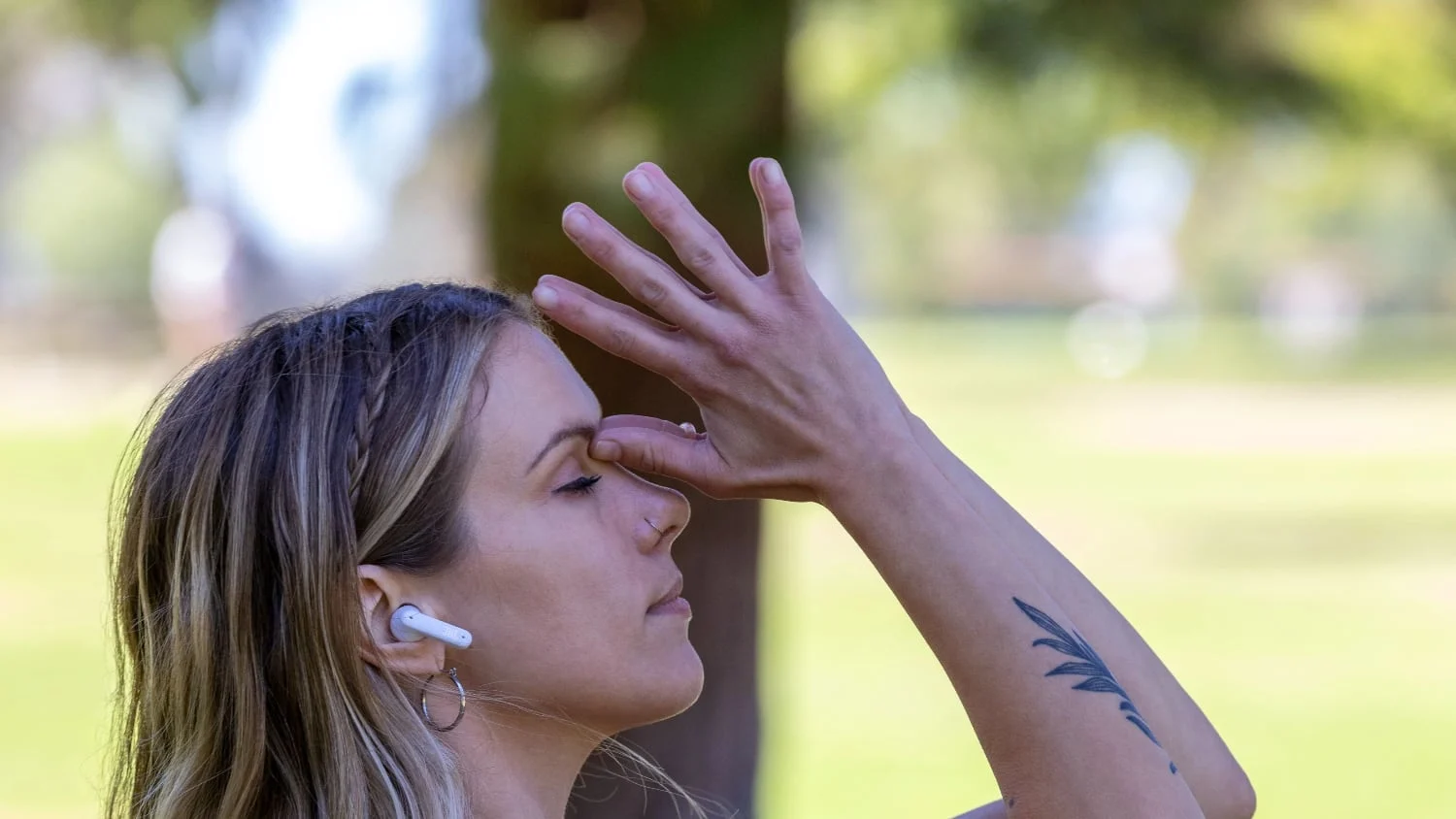 Eine Frau mit weißen JBL Tune Flex Ohrstöpseln beim Yoga oder Tai Chi in einem Park.