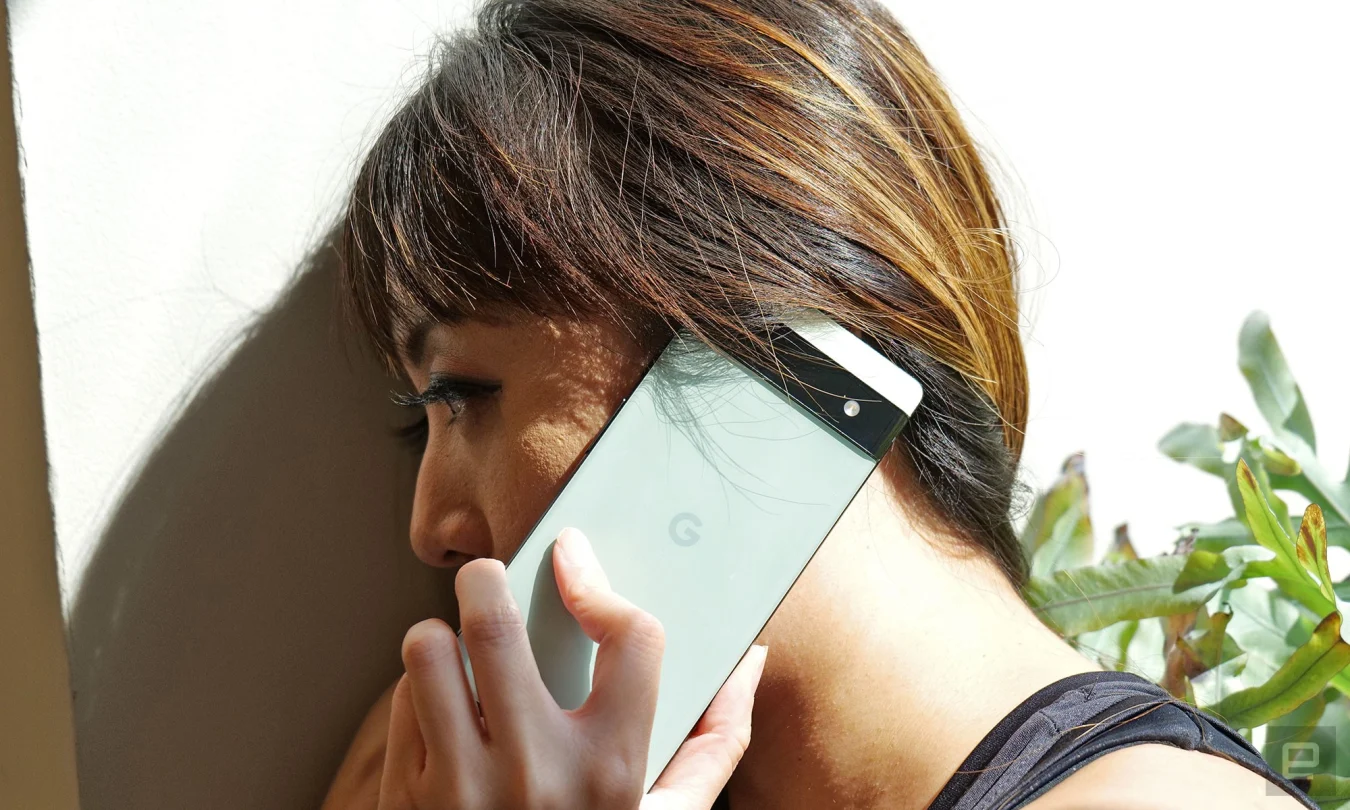 A woman holding up the sage Pixel 6a to her ear.