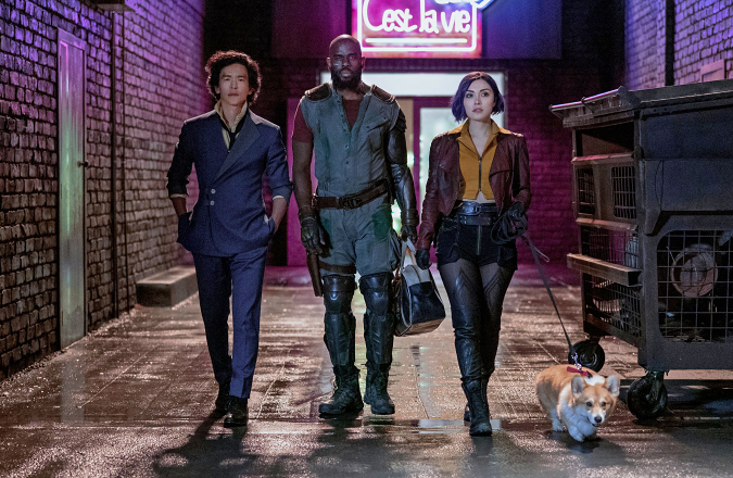 A still promoting the new live-action Netflix series 'Cowboy Bebop' showing three people and a corgi walking down a water-slicked back alley.
