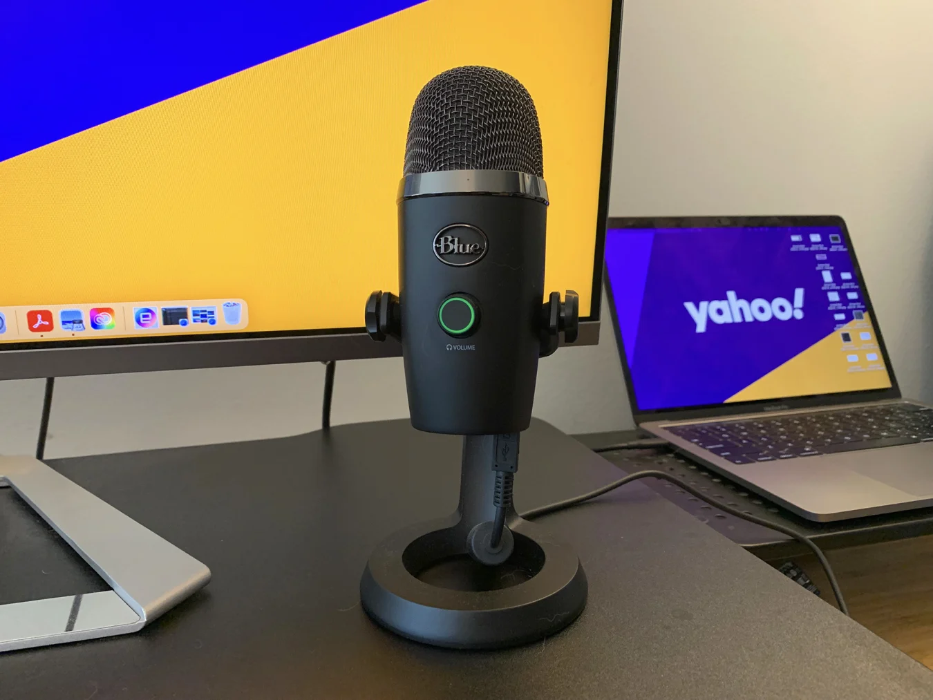 The Blue Yeti Nano microphone on a black desk riser in front of a laptop and a computer monitor.