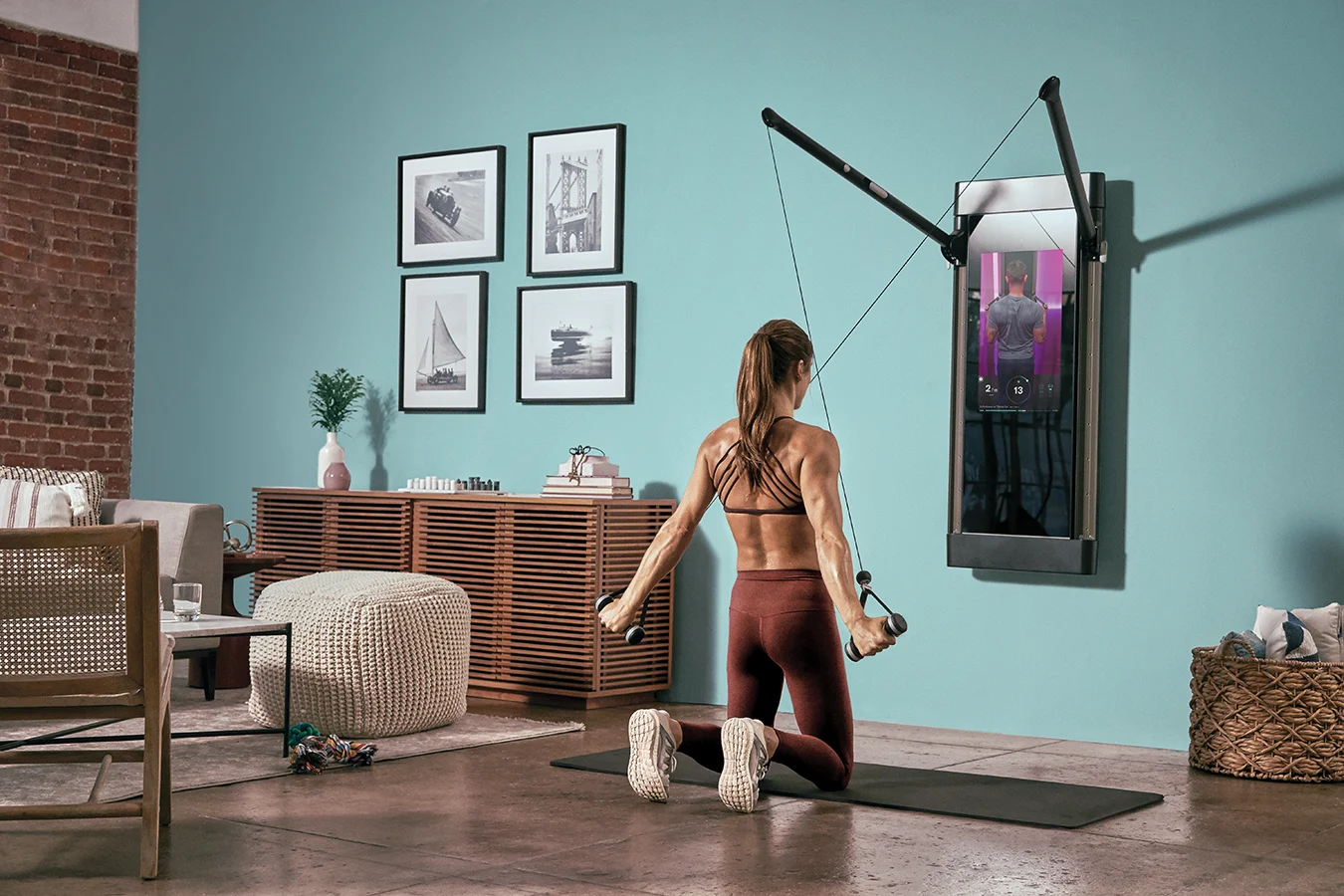 A woman using the Tonal wall-mounted workout system, performing a pulldown. 