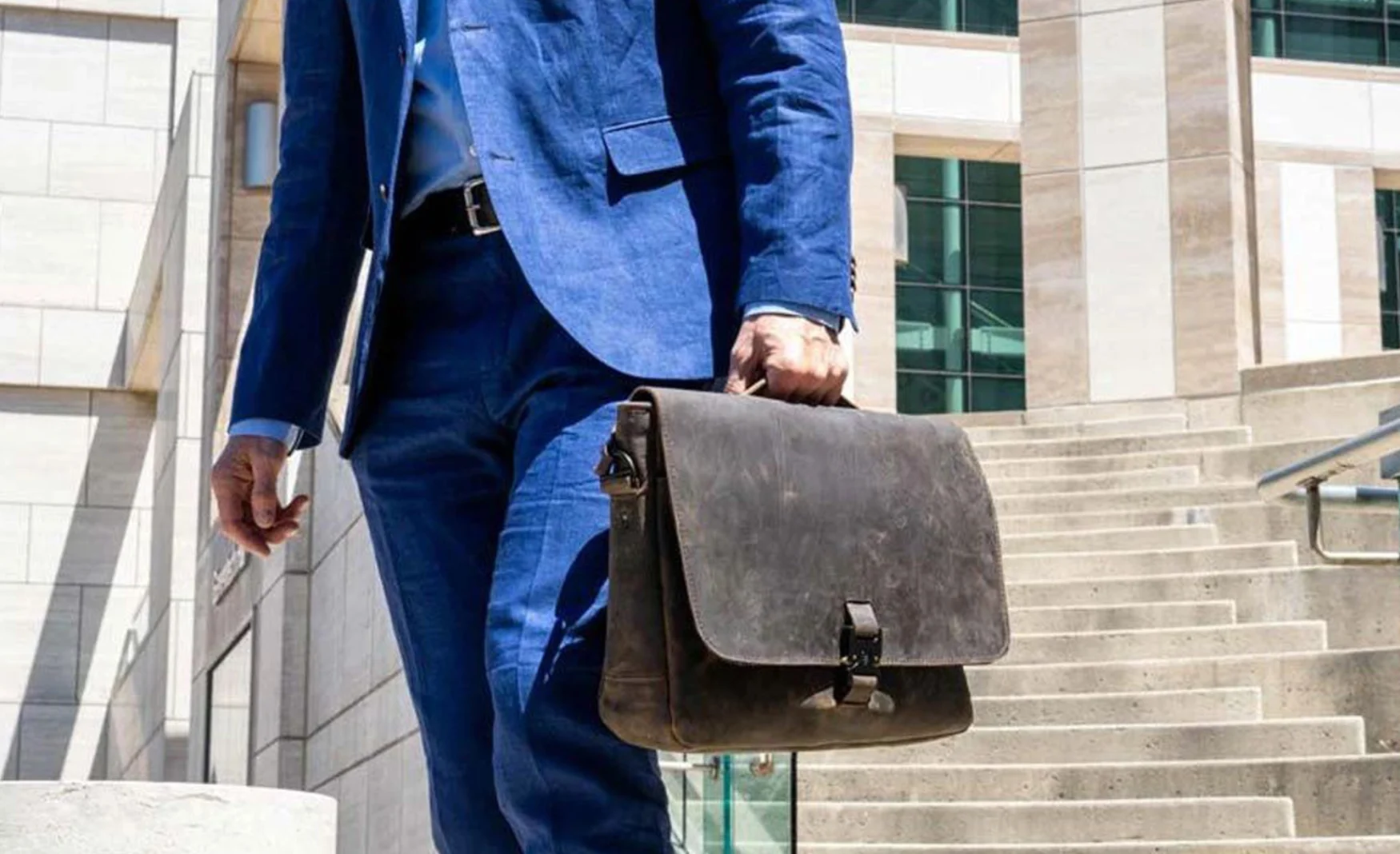 A man in a blue suit holds a brown Waterfield Designs Executive Leather Messenger bag.