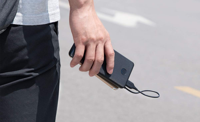 A hand gripping a cellphone that's connected to the Anker PowerCore Slim 10K portable power bank via a cable.