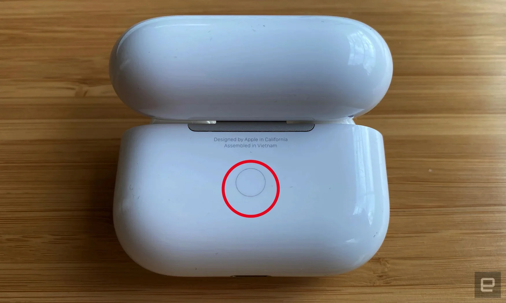 Gambar jarak dekat bagian belakang casing AirPods dengan lingkaran merah di sekitar tombol belakang yang digunakan untuk memasangkan dengan perangkat lain. 