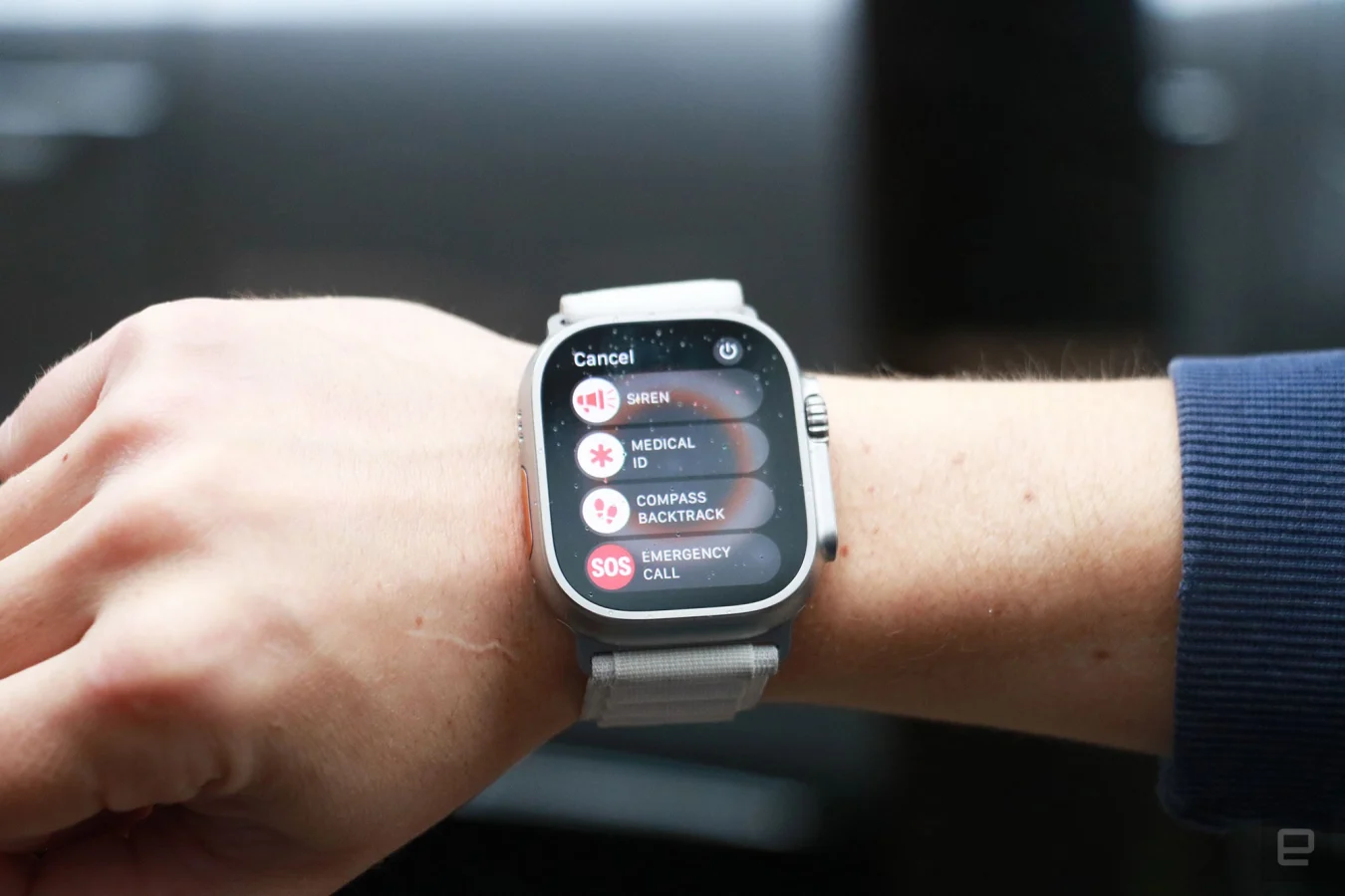 The Apple Watch Ultra with alpine loop on a person's wrist, showing the emergency menu. Options on display are, from top to bottom, Siren, Medical ID, Compass Backtrack and Emergency Call.