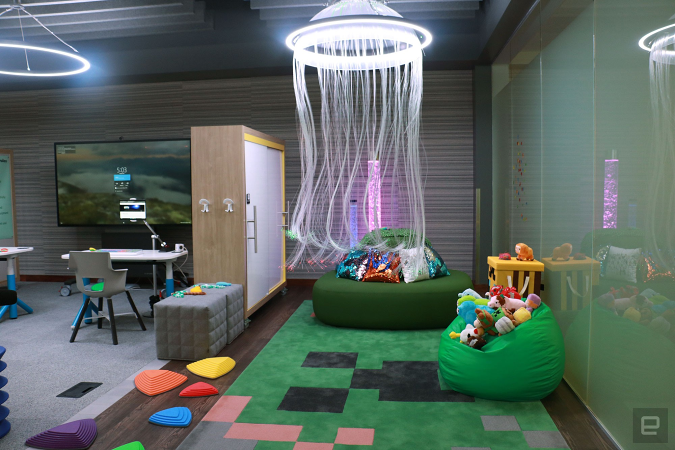 The sensory space inside Microsoft's new Inclusive Tech Lab, with a faux jellyfish suspended from the ceiling. There are green beanbags and chairs in this corner, with piles of colorful plush toys and cushions on them. In the back, along the wall, are a pair of bubbling lamps.